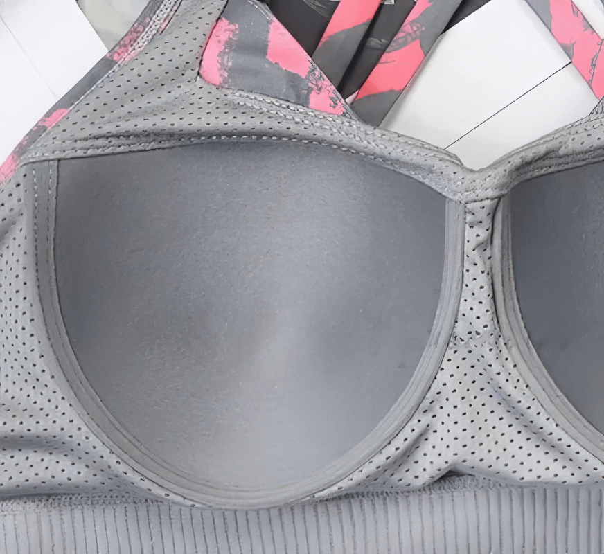Close-up of a stylish elastic sports bra with cross back for women, featuring breathable grey fabric and pink accents. Model SF1610.
